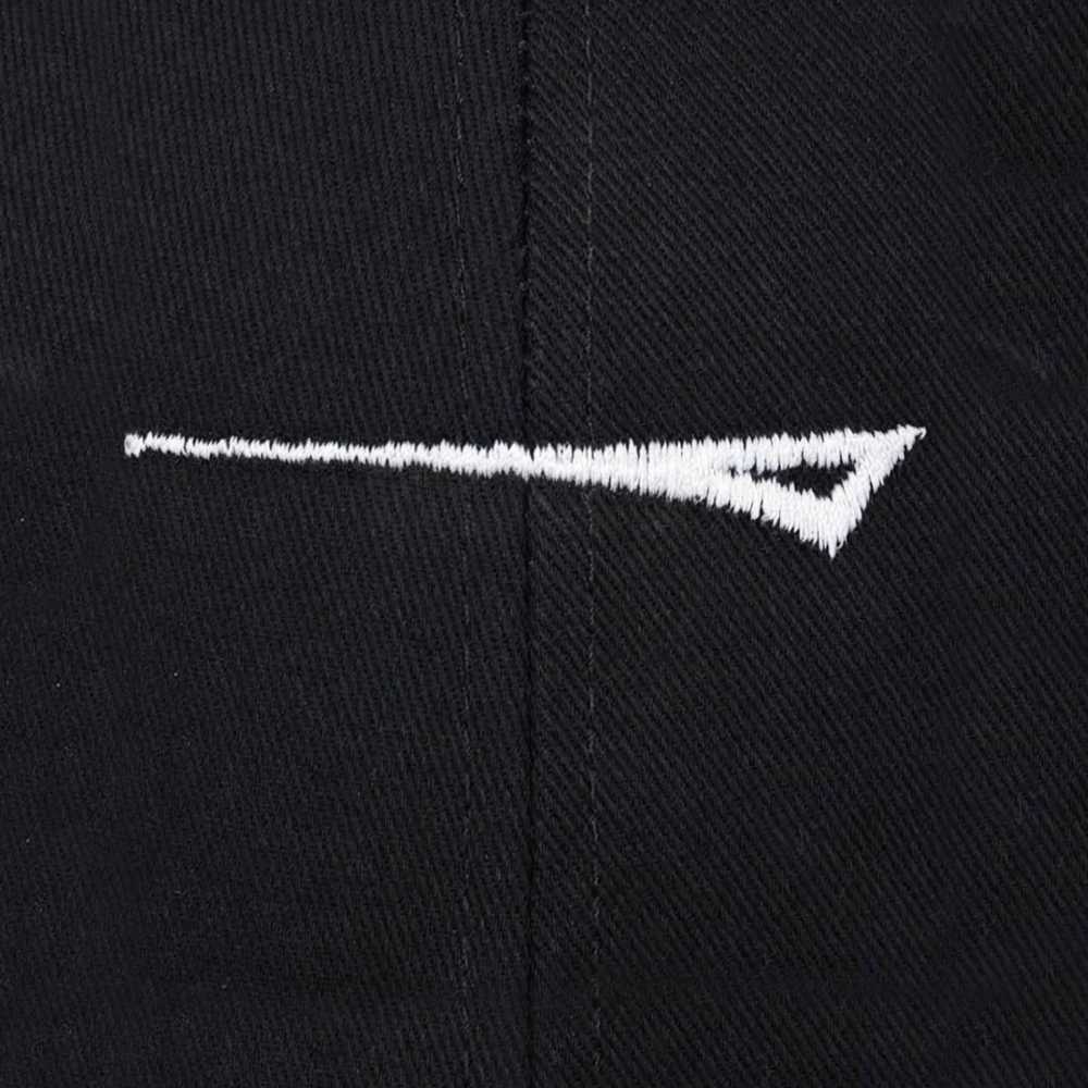 Close-up of a black fabric surface with a white embroidered abstract logo or mark across the center.
